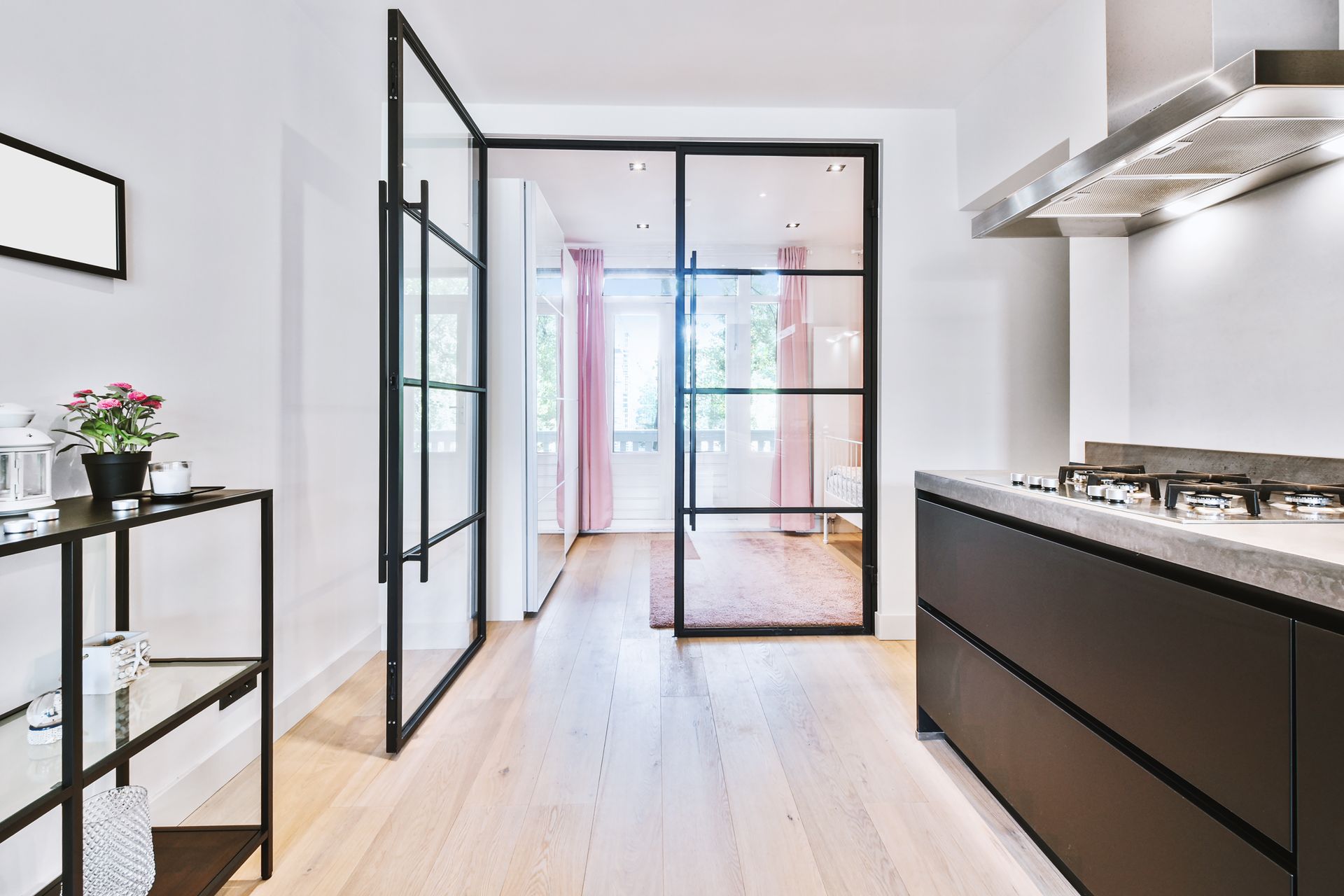 Modern kitchen with black framed glass doors leading to a room with pink curtains; black cabinet and steel range hood. Modern kitchen with black framed glass doors leading to a room with pink curtains; black cabinet and steel range hood.