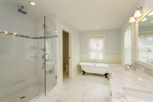 Spacious bathroom with glass shower, clawfoot tub, and marble countertops, white and light blue color scheme.