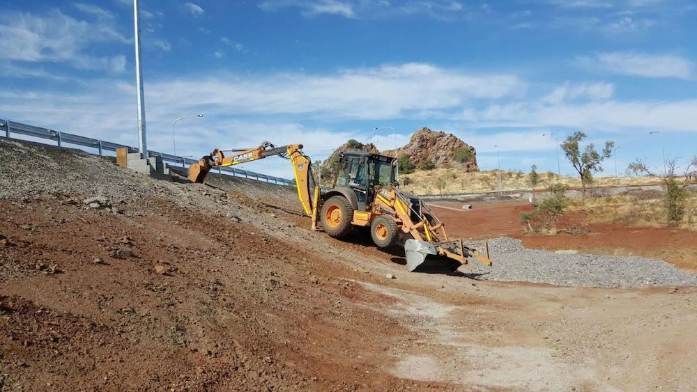 Yellow Backhoe Digging on a Slope, Near a Roadway and Rocky Landscape — Lamont Civil Services Pty Ltd In Townview, QLD