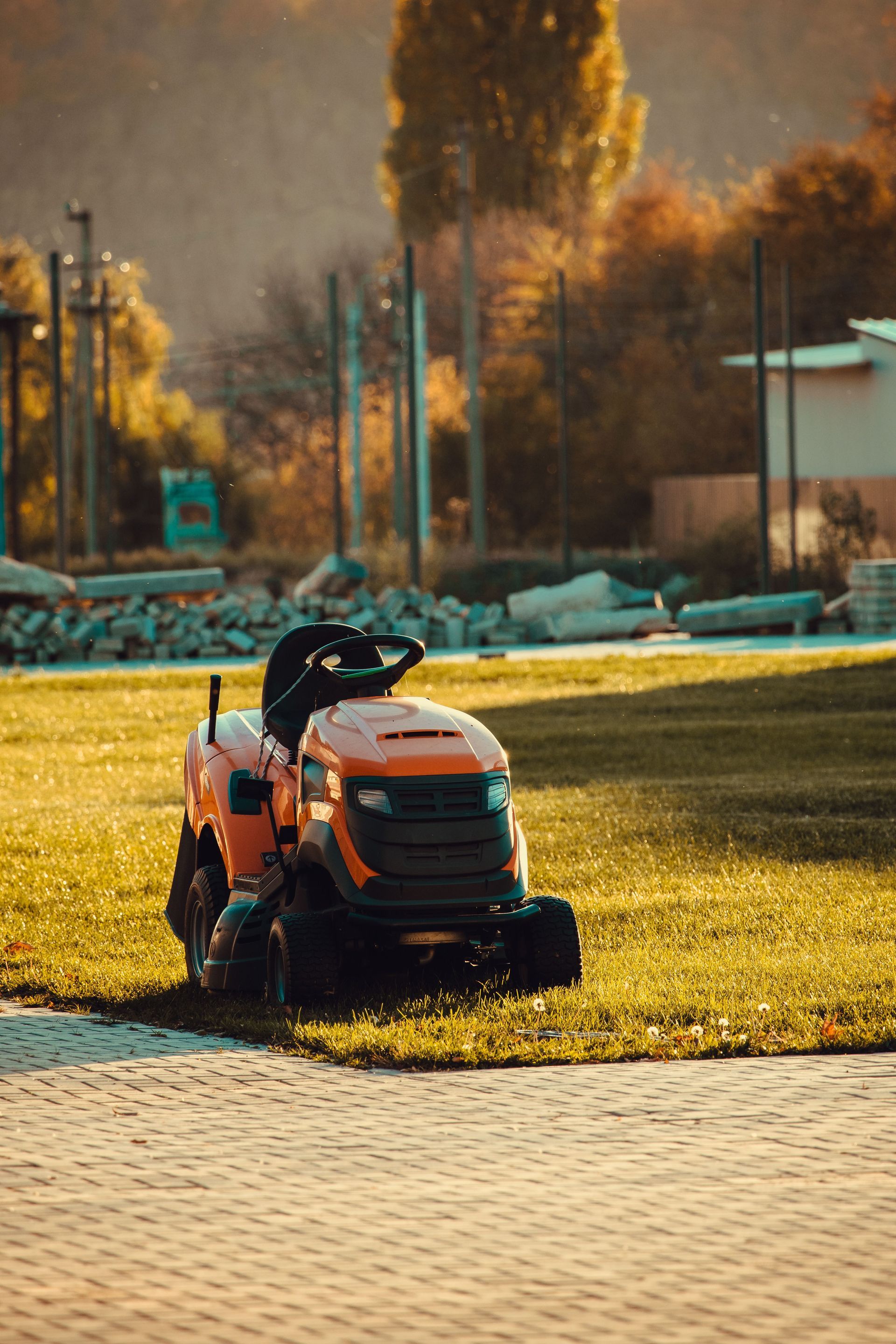 Orange lawn tractor on grass near a paved path in a park at sunset