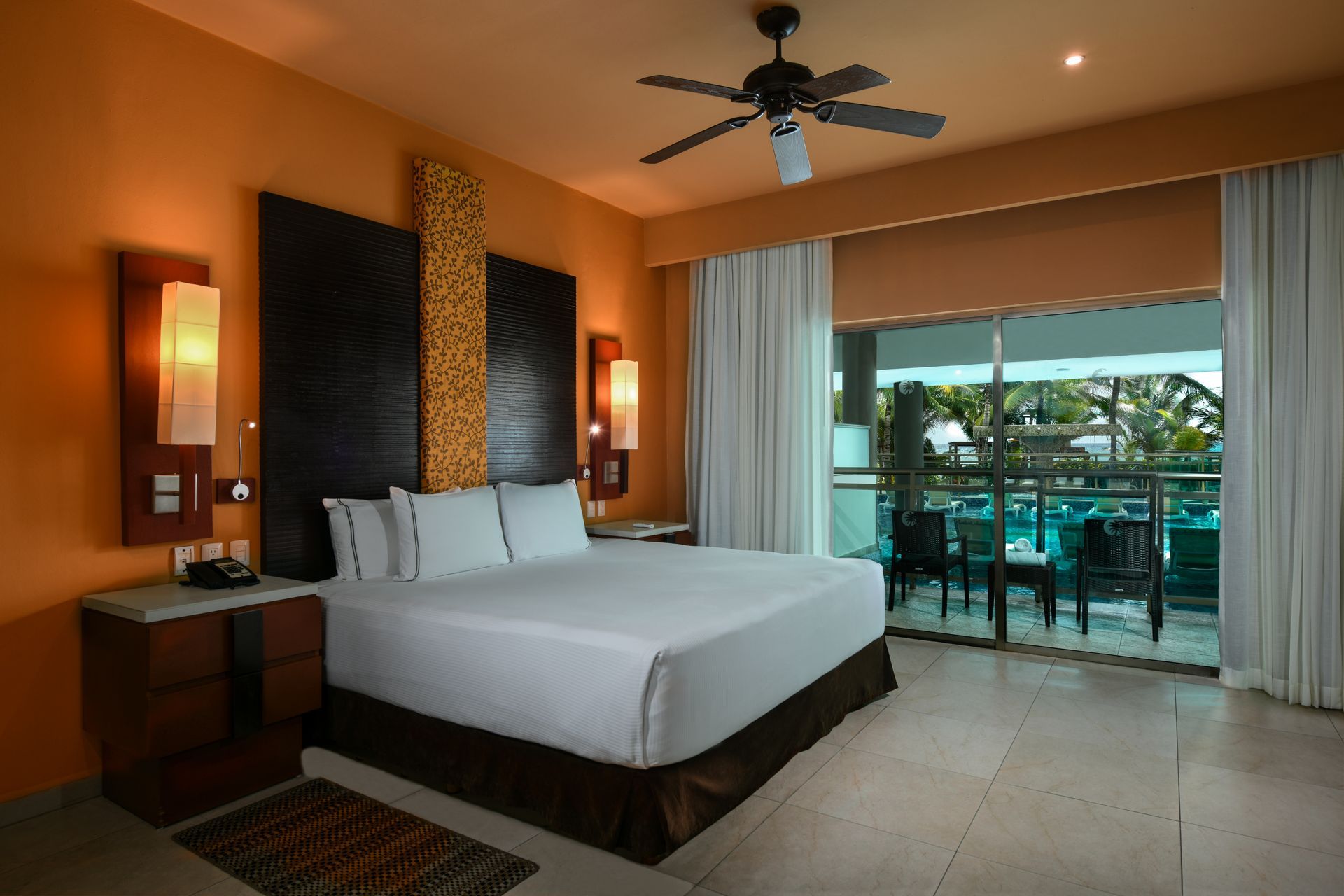 Hotel bedroom with king bed, orange walls, balcony overlooking pool.