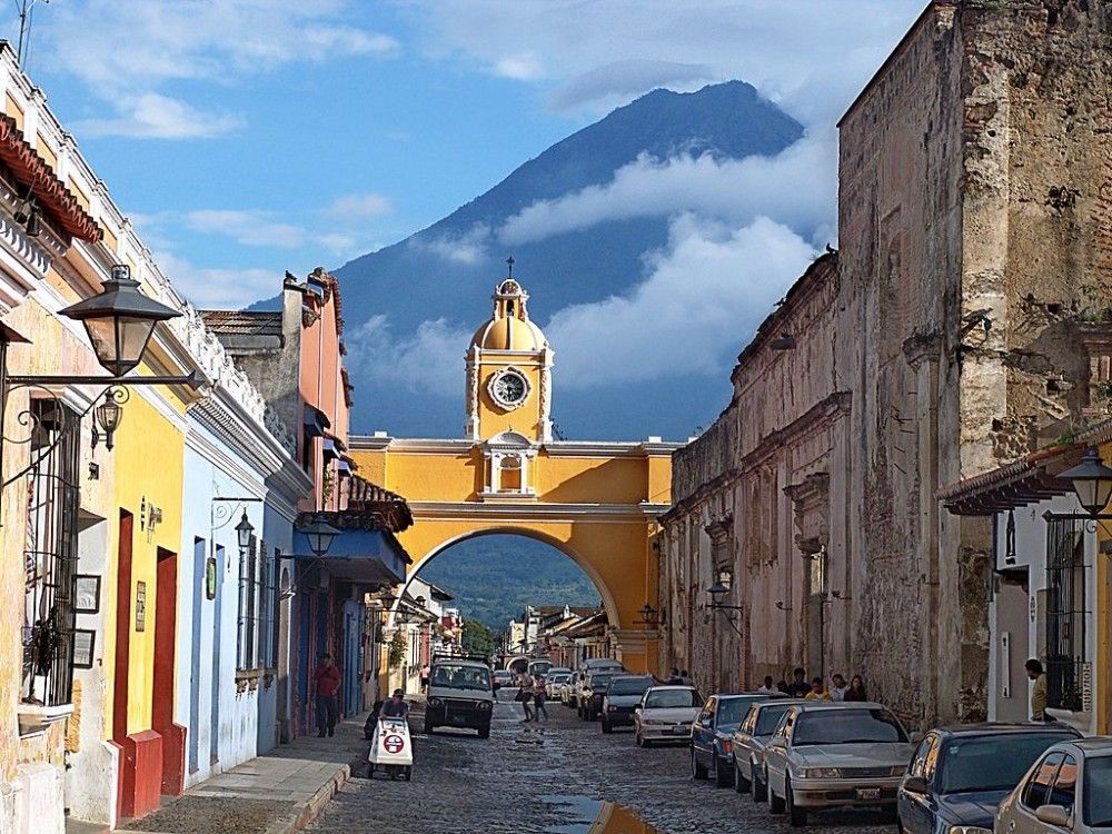 Street scene in Antigua, Guatemala, featuring the Santa Catalina Arch with Volcán de Agua in the background.