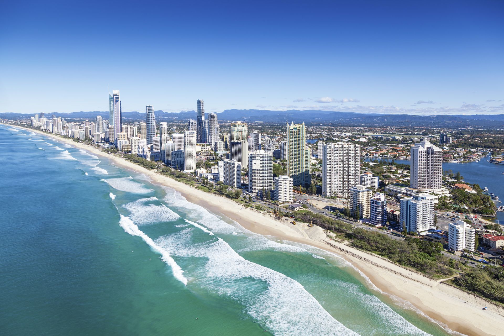 Coastal city skyline along a sandy beach with turquoise water on a sunny day.