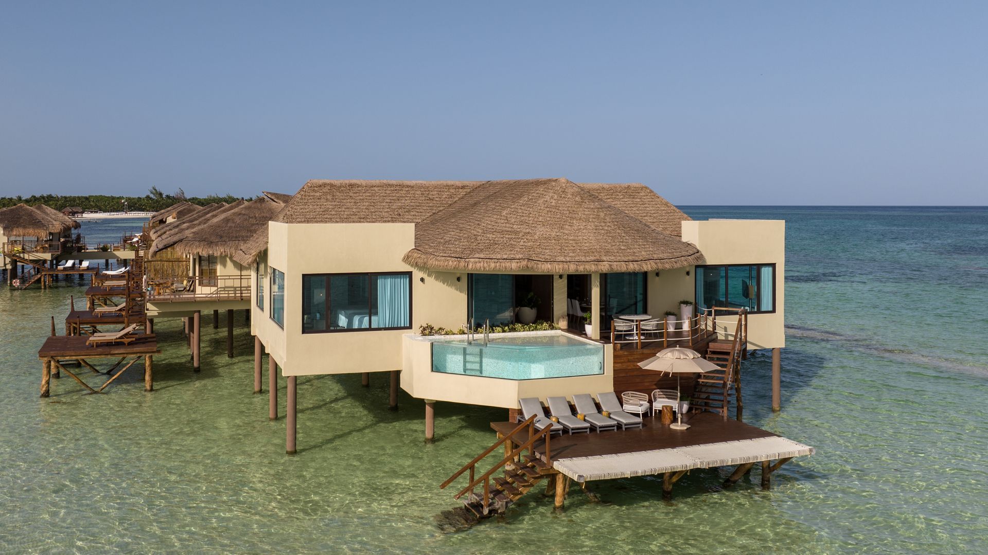 Overwater bungalow with thatched roof and private pool in turquoise water.