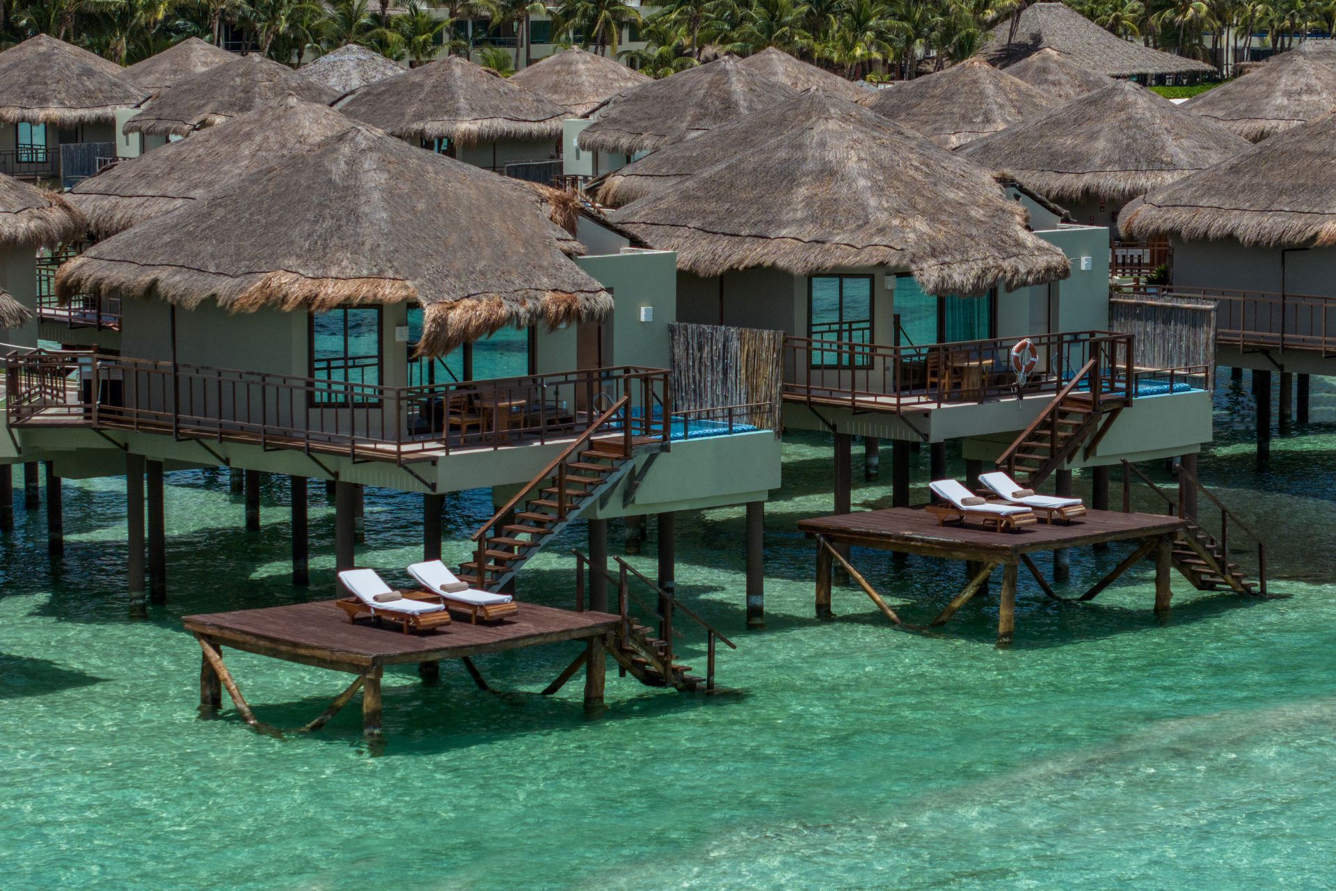 Overwater bungalows with thatched roofs in clear turquoise water.