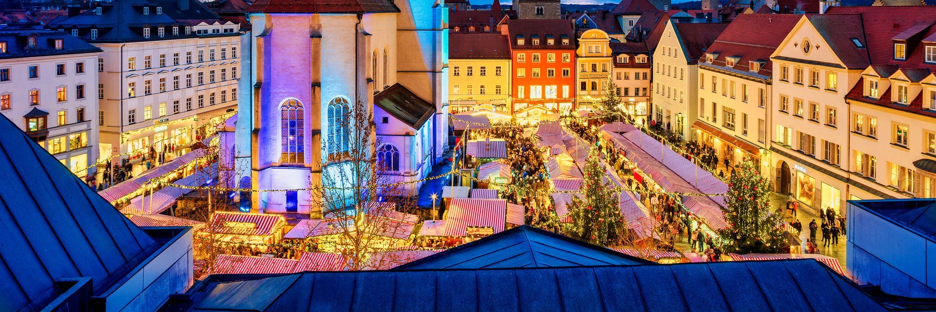 Aerial view of a Christmas market in a European city at night, with colorful lights and buildings.