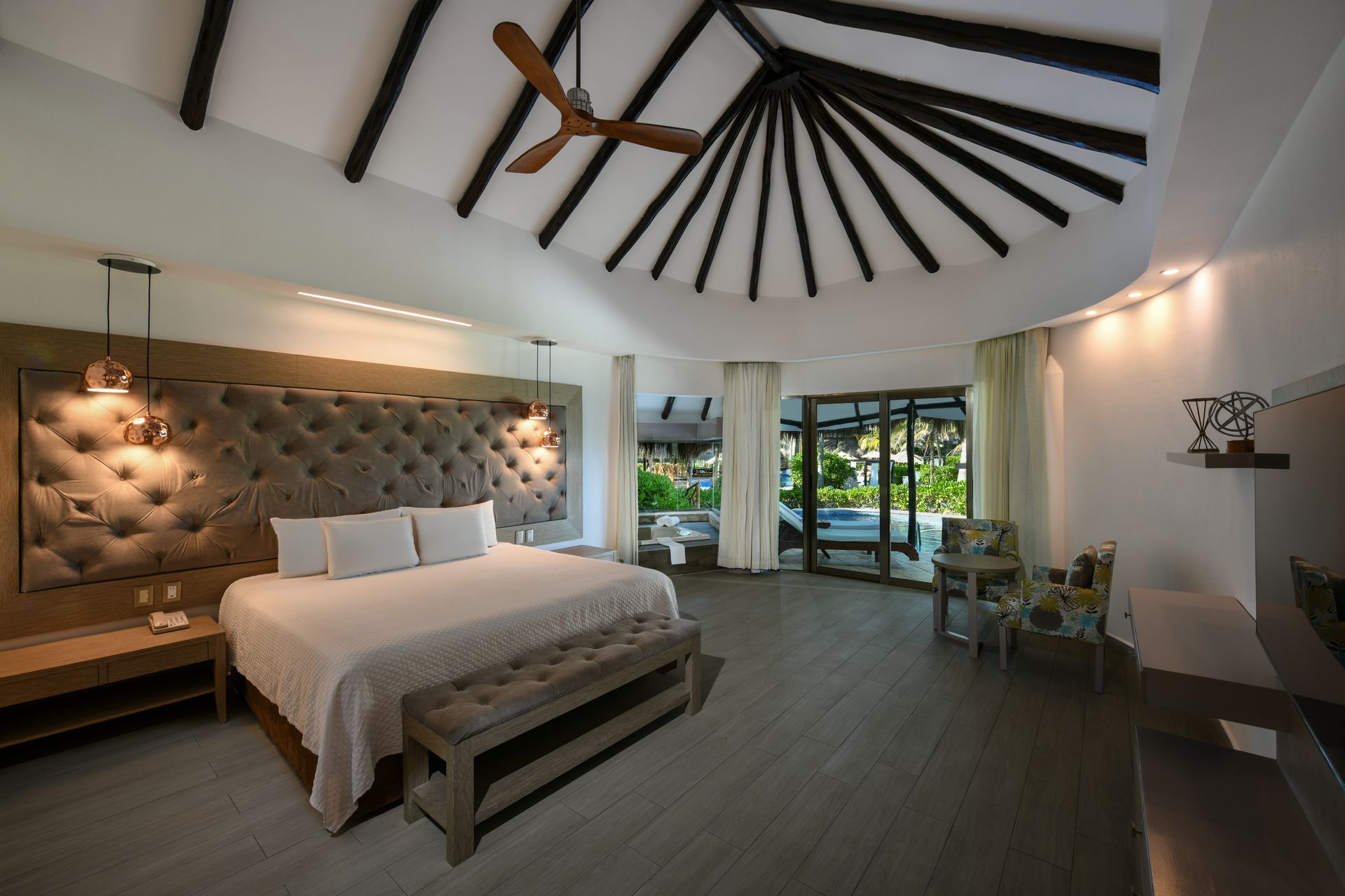 Spacious hotel bedroom with king bed, high ceiling, and sliding doors to a pool area.
