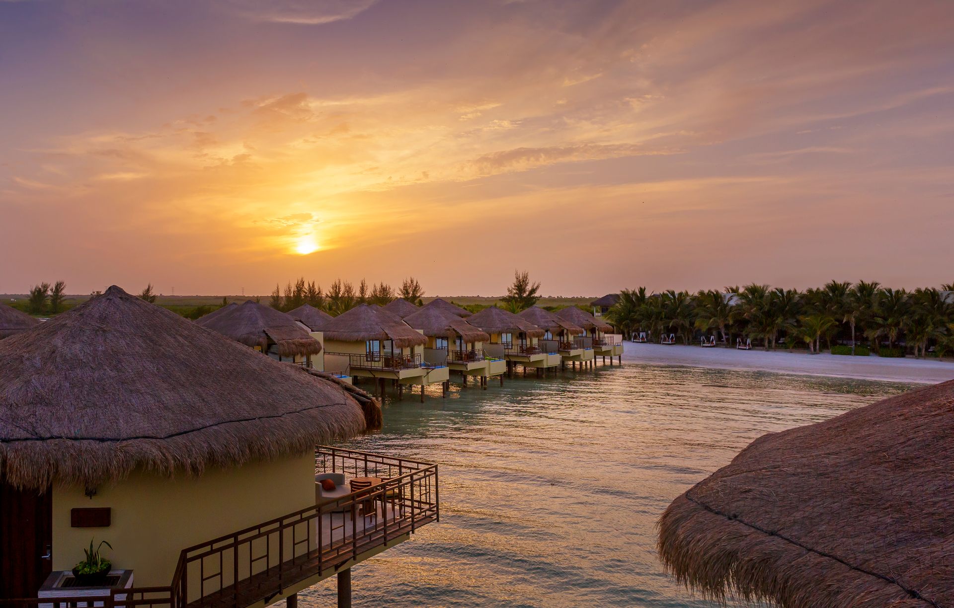 Overwater bungalows at sunset with a golden sky reflecting on the water.