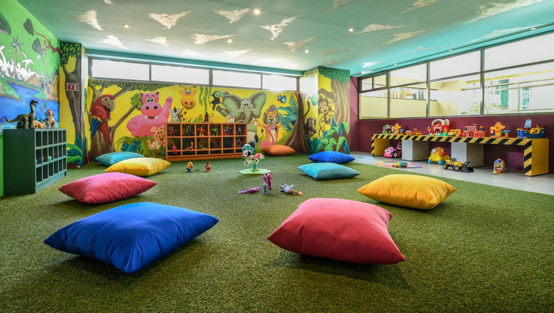 Playroom with colorful bean bags on green carpet, mural, toys, and windows.