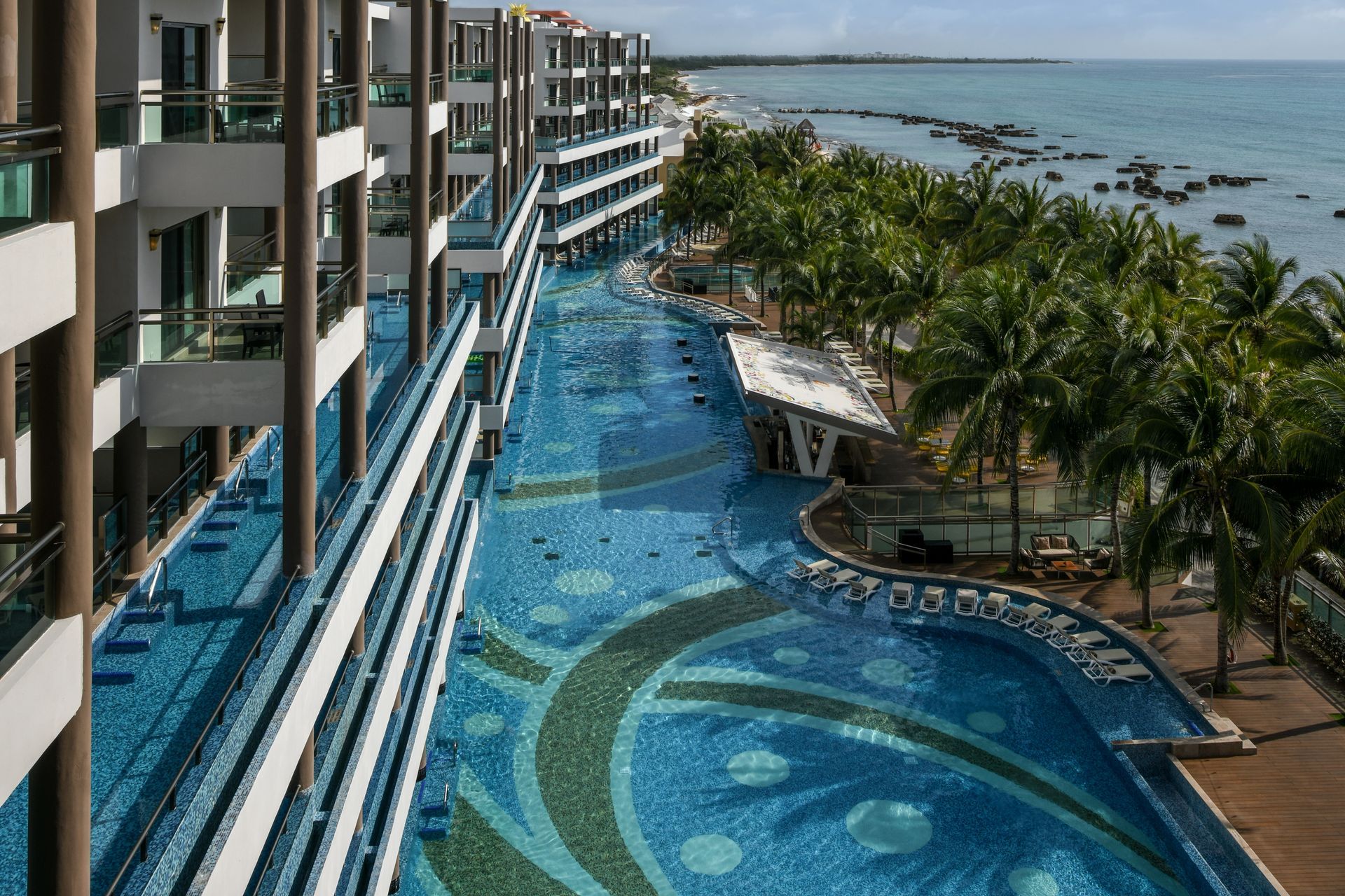 Long resort pool and oceanfront hotel with palm trees.