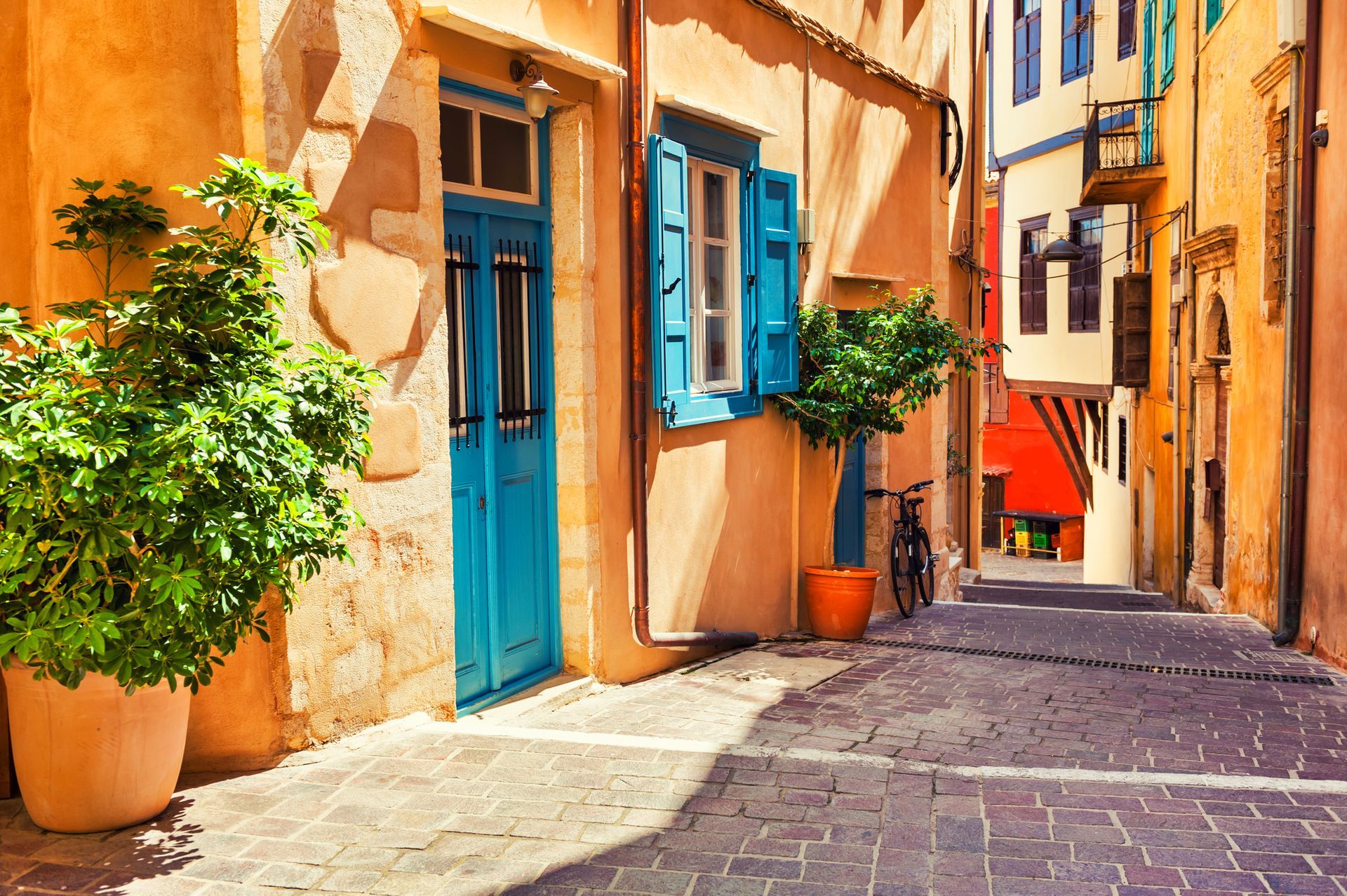 Narrow cobblestone street with colorful buildings: turquoise door, orange walls, potted plants.