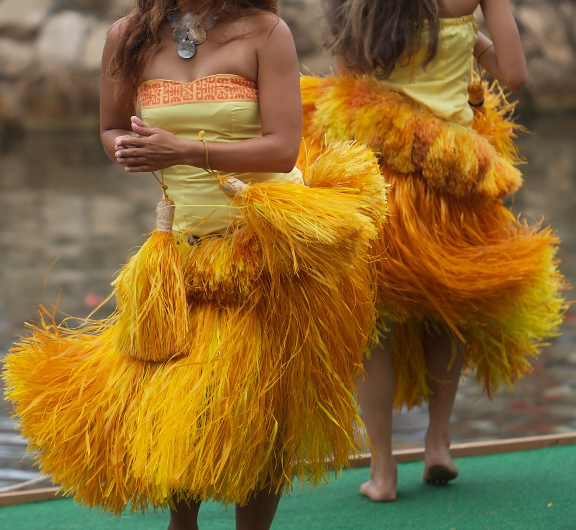 Two women in yellow dresses with orange fringe dancing outdoors.
