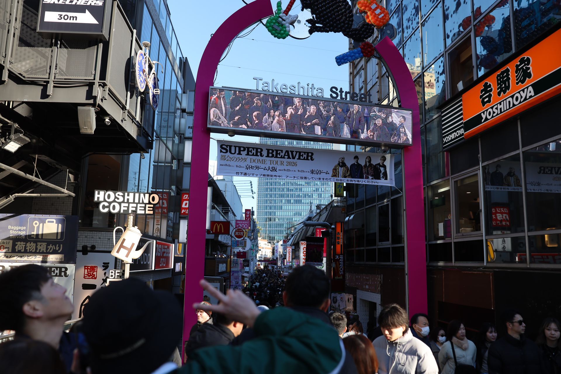Crowds walking beneath Takeshita Street entrance in Harajuku, Tokyo, a vibrant hub for street fashio