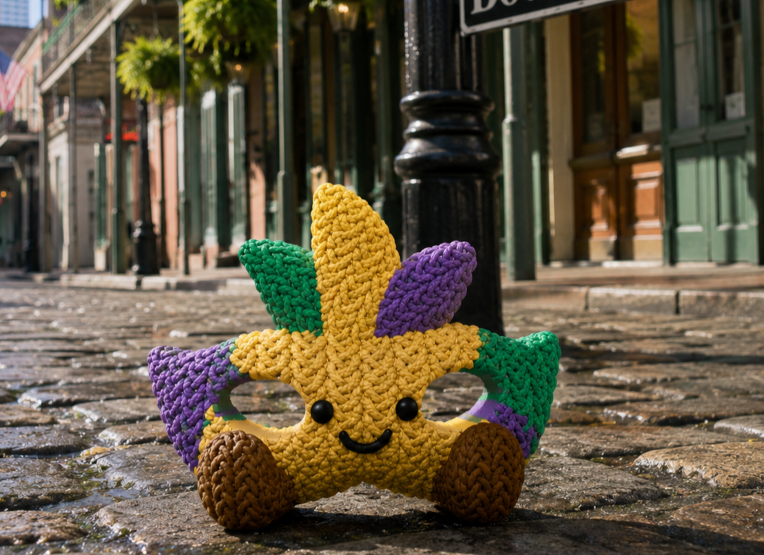 Mardi the Mask, a colorful crochet-style Mardi Gras mask Buddy celebrating on Bourbon Street in New Orleans.