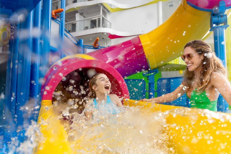 Woman slides down colorful waterslide as friend laughs, both in a water park setting.