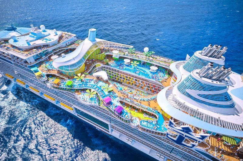 Aerial view of a colorful cruise ship deck with water slides, pools, and recreational areas on the ocean.