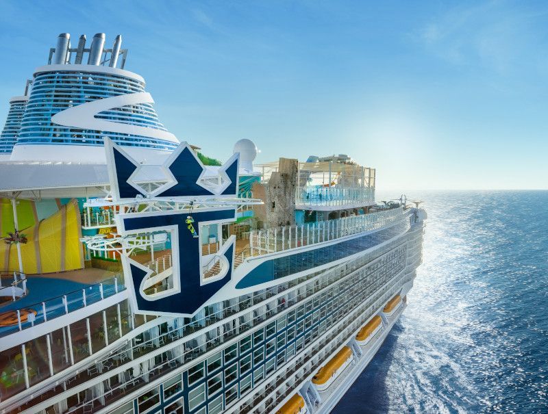 Large cruise ship sailing on a sunny day, logo of Royal Caribbean visible.