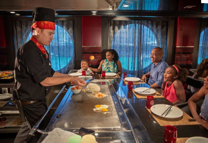 Chef cooking at a teppanyaki grill for a family. Eggs flipping in the air. Restaurant setting.