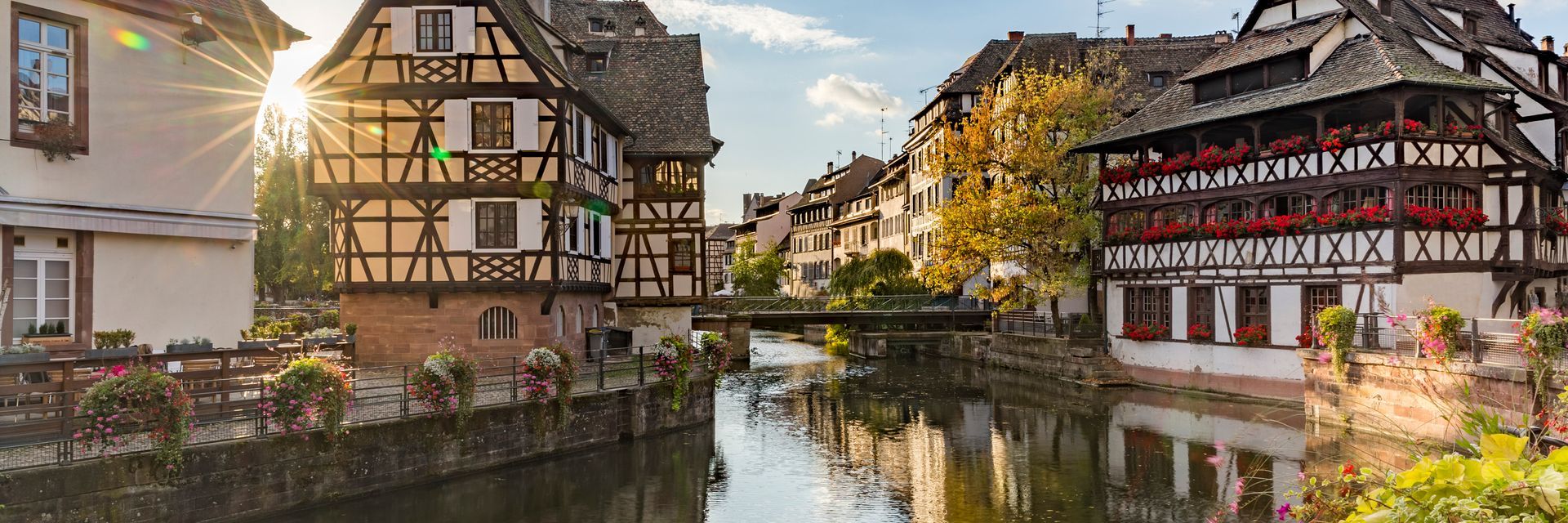 Half-timbered buildings line a canal in Strasbourg, France, with the sun shining.