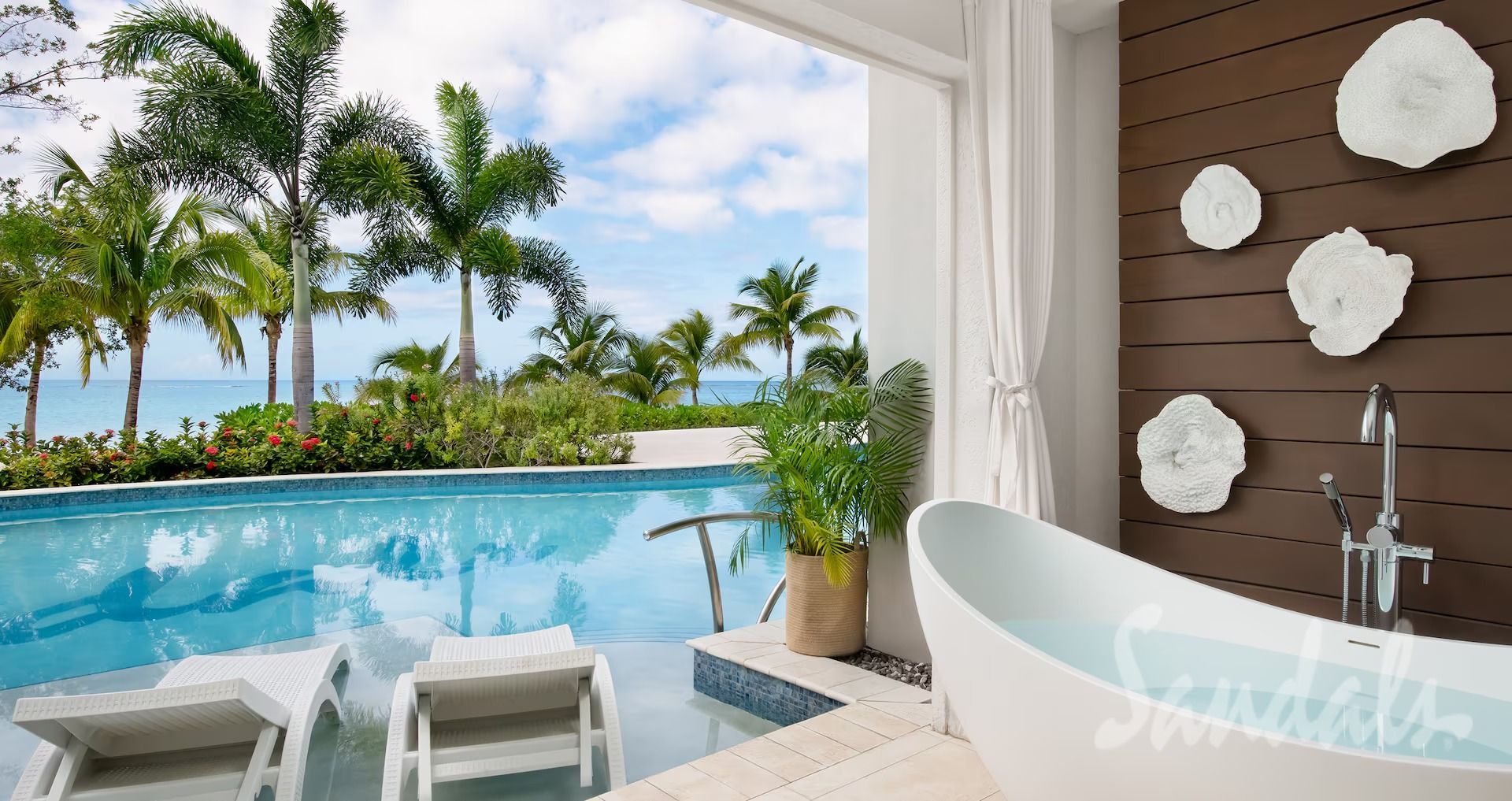 Luxury bathroom with pool view: white tub, lounge chairs, blue water, palm trees, and ocean.