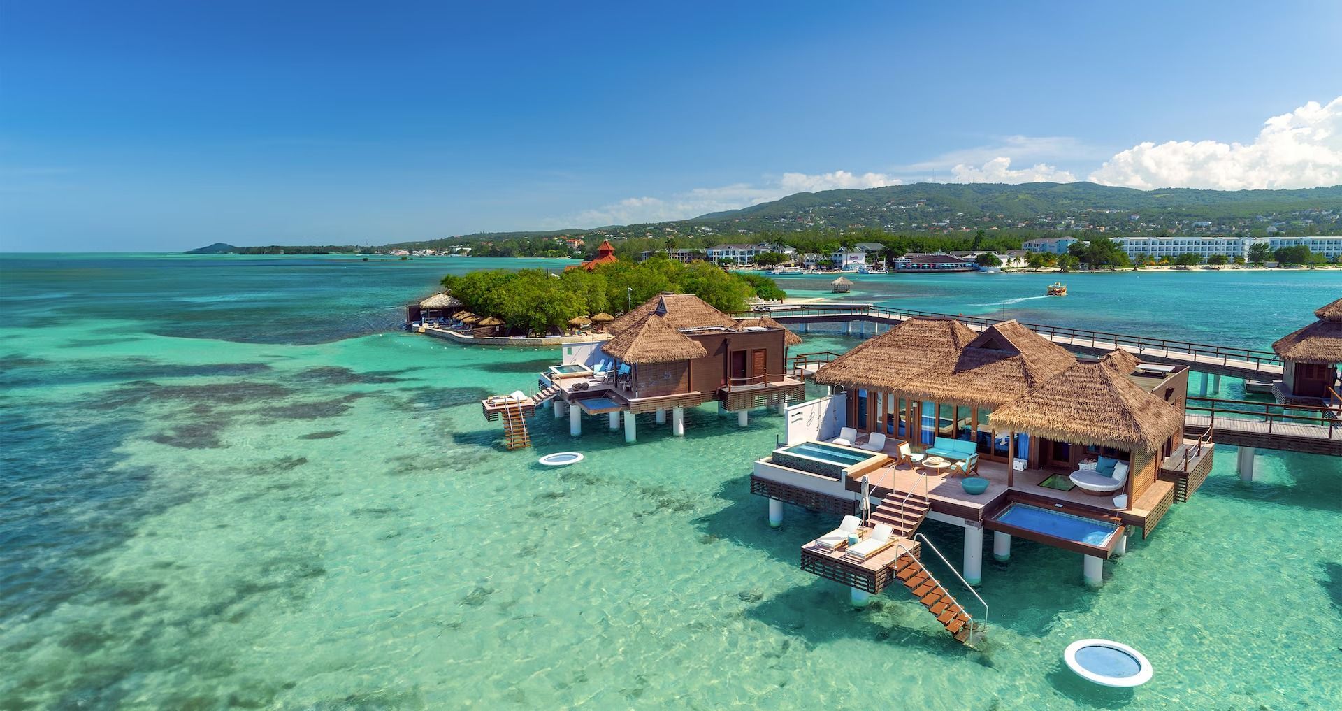 Overwater bungalows in turquoise water, Jamaica. Wooden structures with thatched roofs, blue sky.