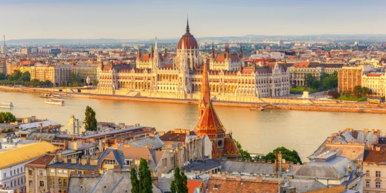 Aerial view of Budapest, Hungary. The Parliament building stands on the riverbank, with boats and city buildings nearby.