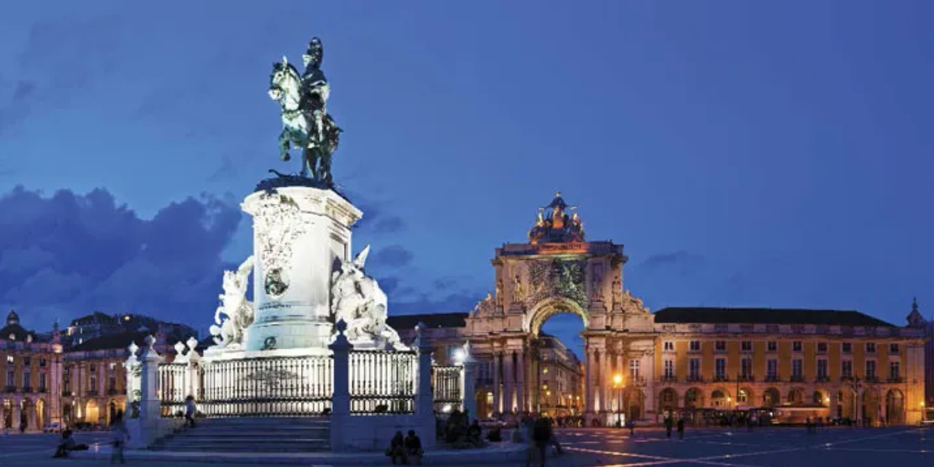 Nighttime view of Praça do Comércio in Lisbon, Portugal, with illuminated monuments and a statue of King Joseph I.