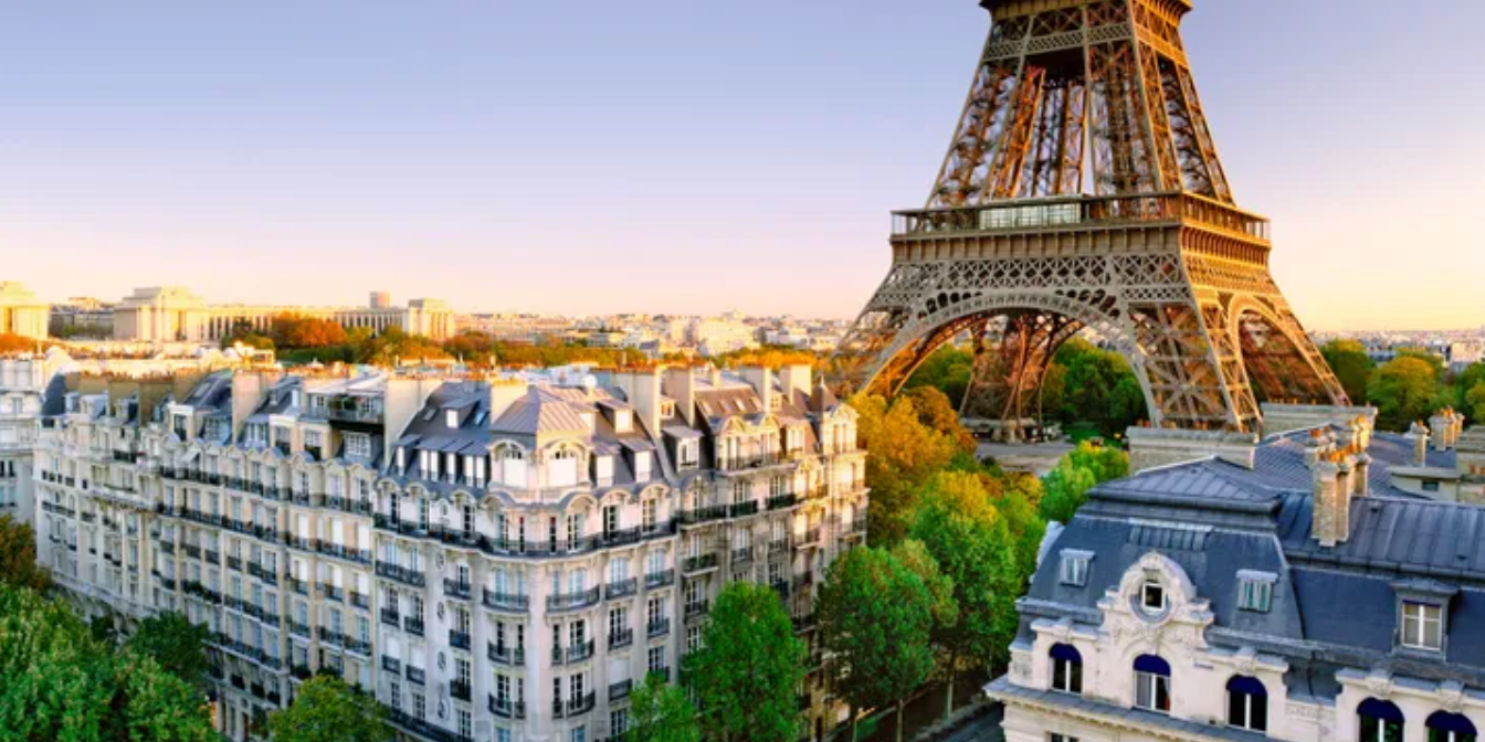 Eiffel Tower in Paris, France, surrounded by buildings and trees under a clear sky at sunset.