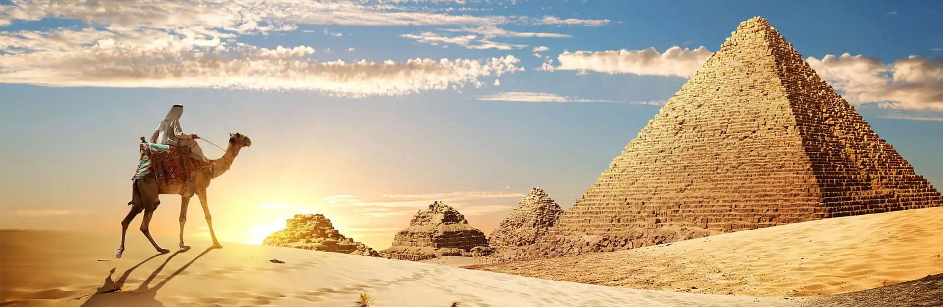 Person riding a camel in front of the pyramids at sunset in Egypt.