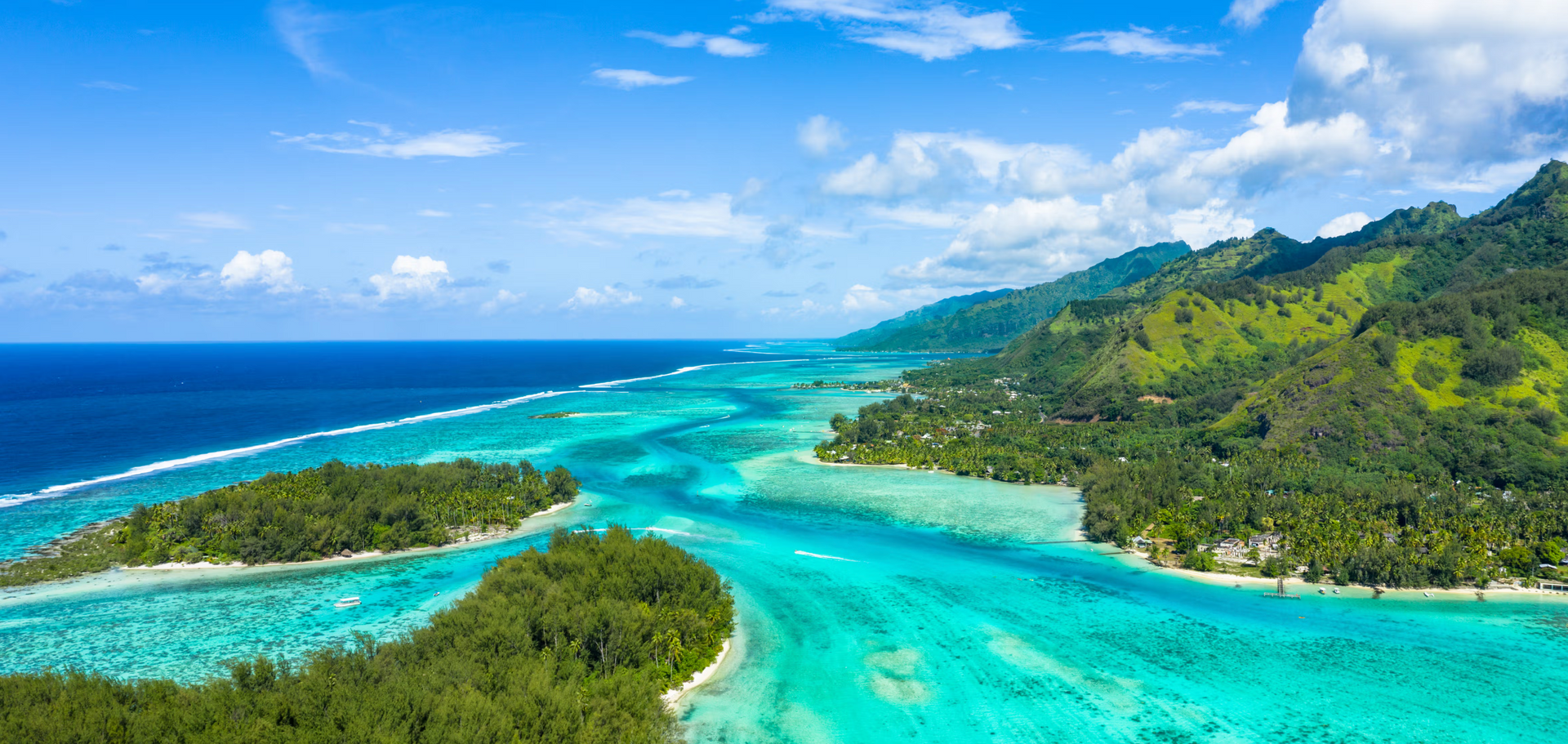 Turquoise lagoon with islands, green hills, blue sky, and white clouds.