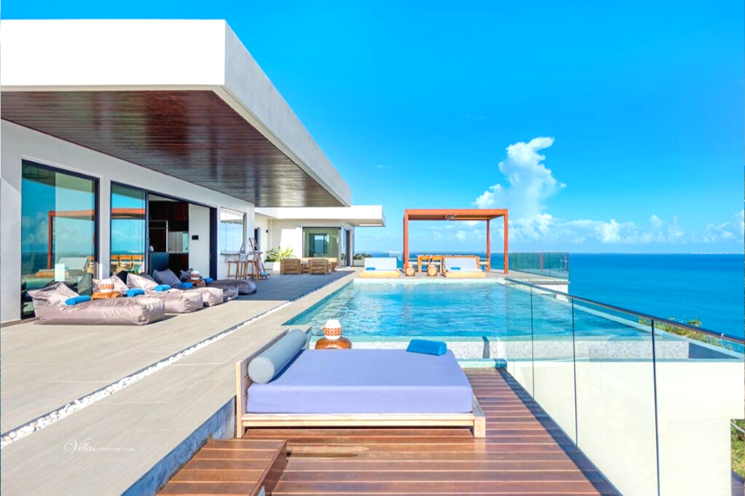 Modern beachfront villa with infinity pool, deck, blue ocean, and sky.