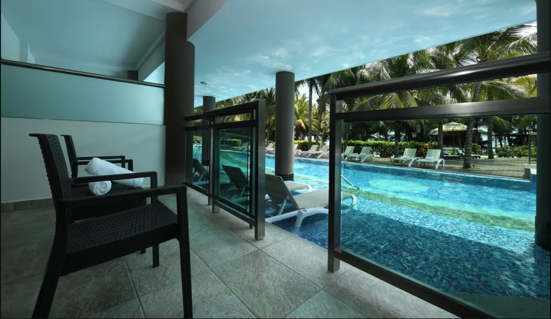 Rolled brown towels with swimming goggles overlooking a pool and beach.