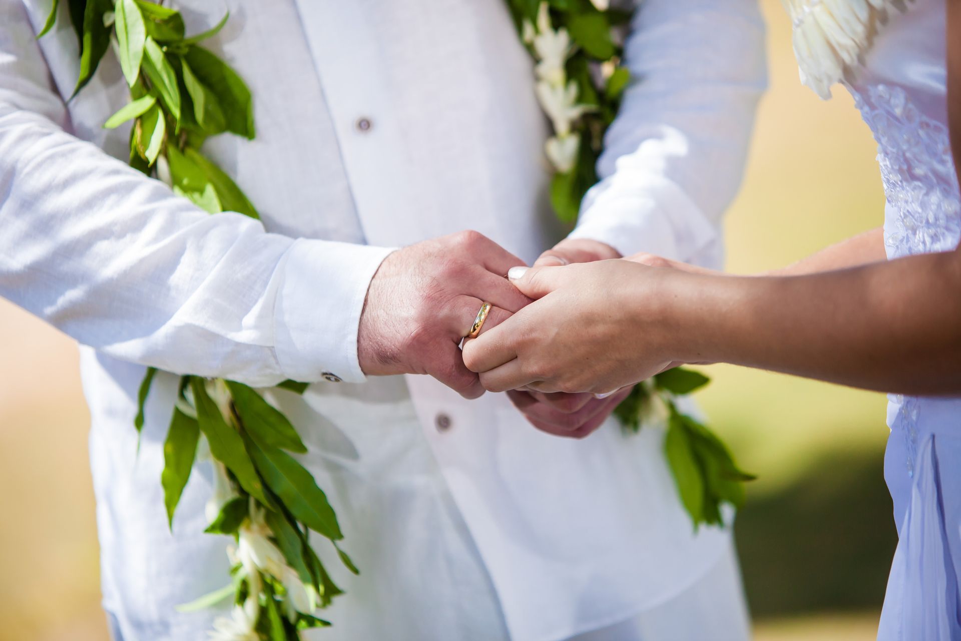 Couple holding hands, one wearing a garland, exchanging rings outdoors.