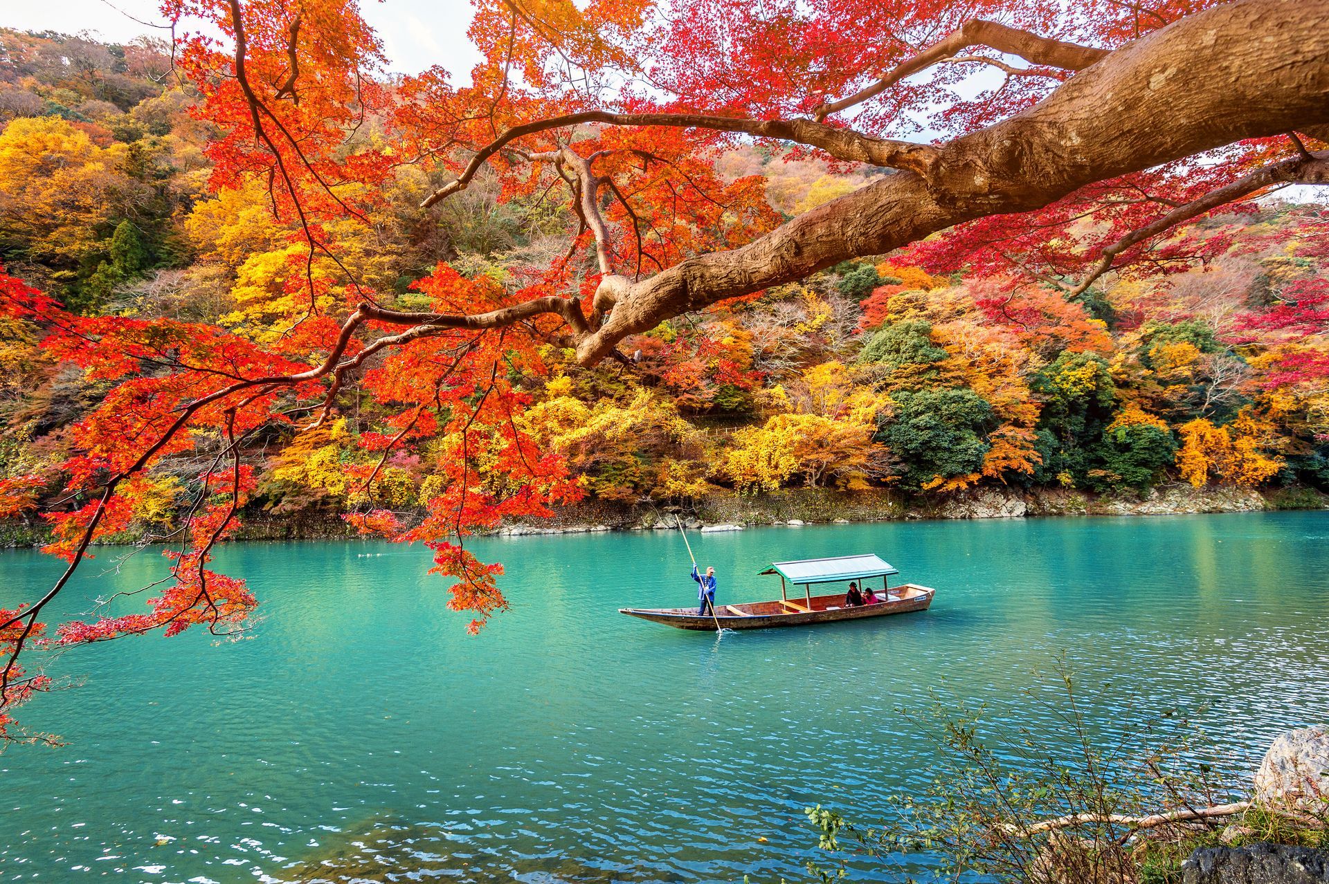 Boat on turquoise water under colorful autumn trees.