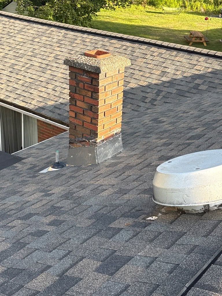 Rooftop with a brick chimney and white vent on gray shingles.