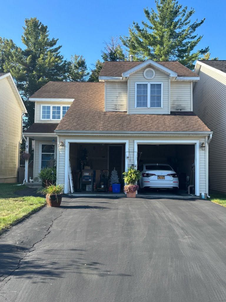 Suburban house with two-car garage, dark driveway, and a white car parked inside one bay