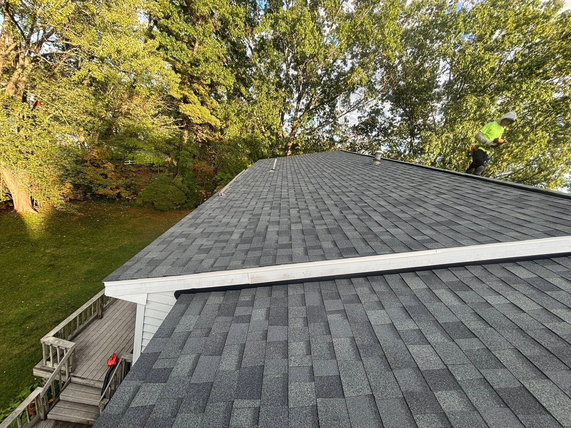 Gray shingled roof viewed from above, with trees and a deck railing along the left side.