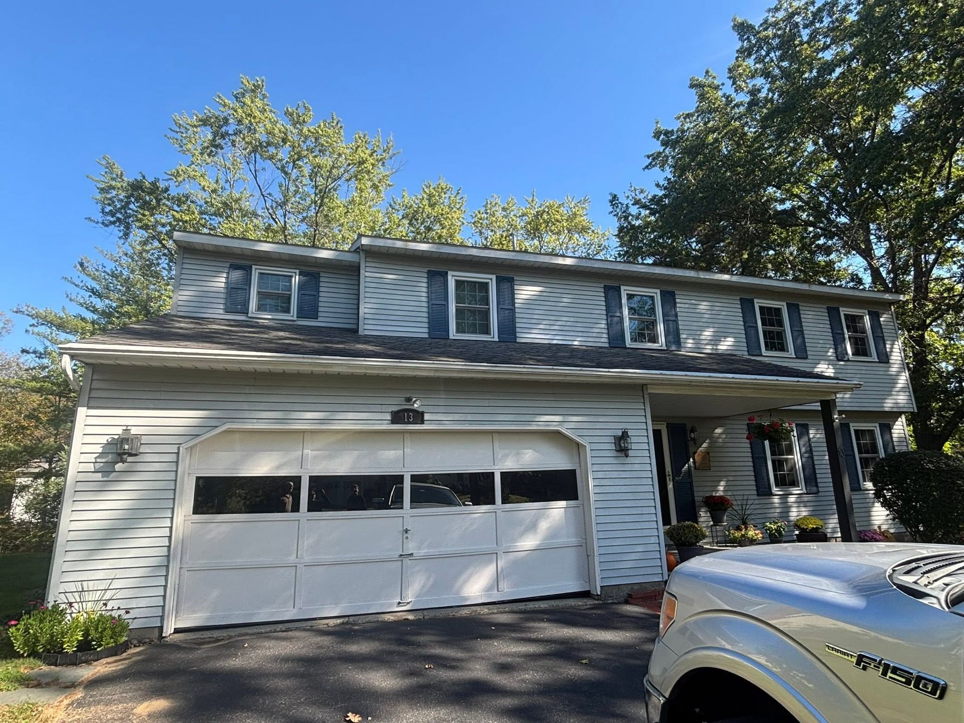 Suburban two-story house with white garage, gray siding, and a truck parked in front under a blue sky