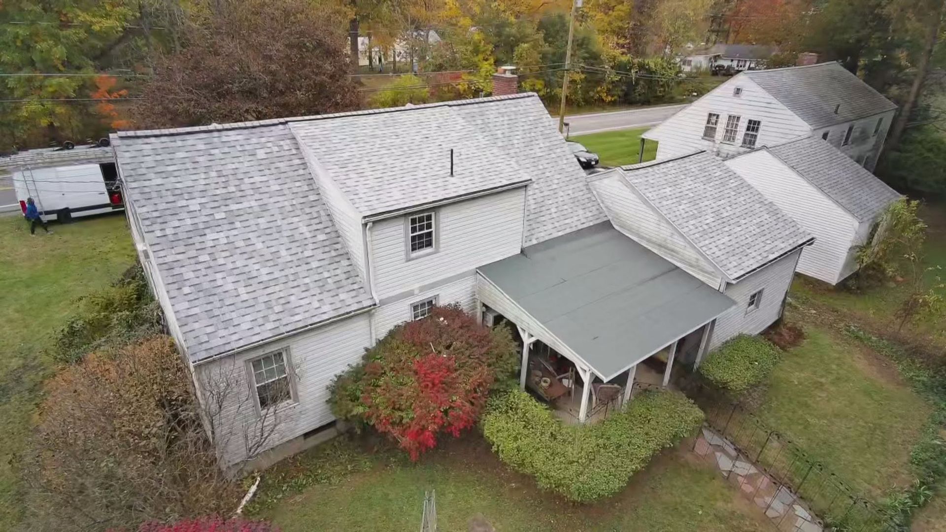 Aerial view of a white house with gray roof, covered porch, and autumn trees in the yard.