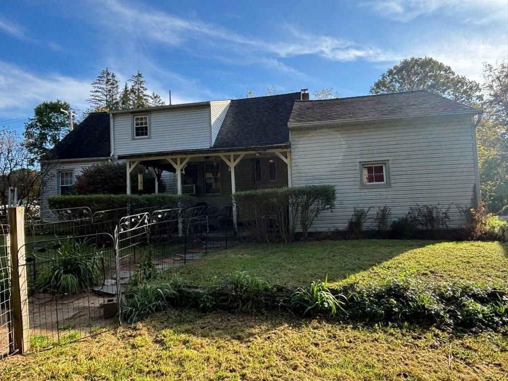 Small white house with a dark roof, front porch, and fenced yard in sunlight