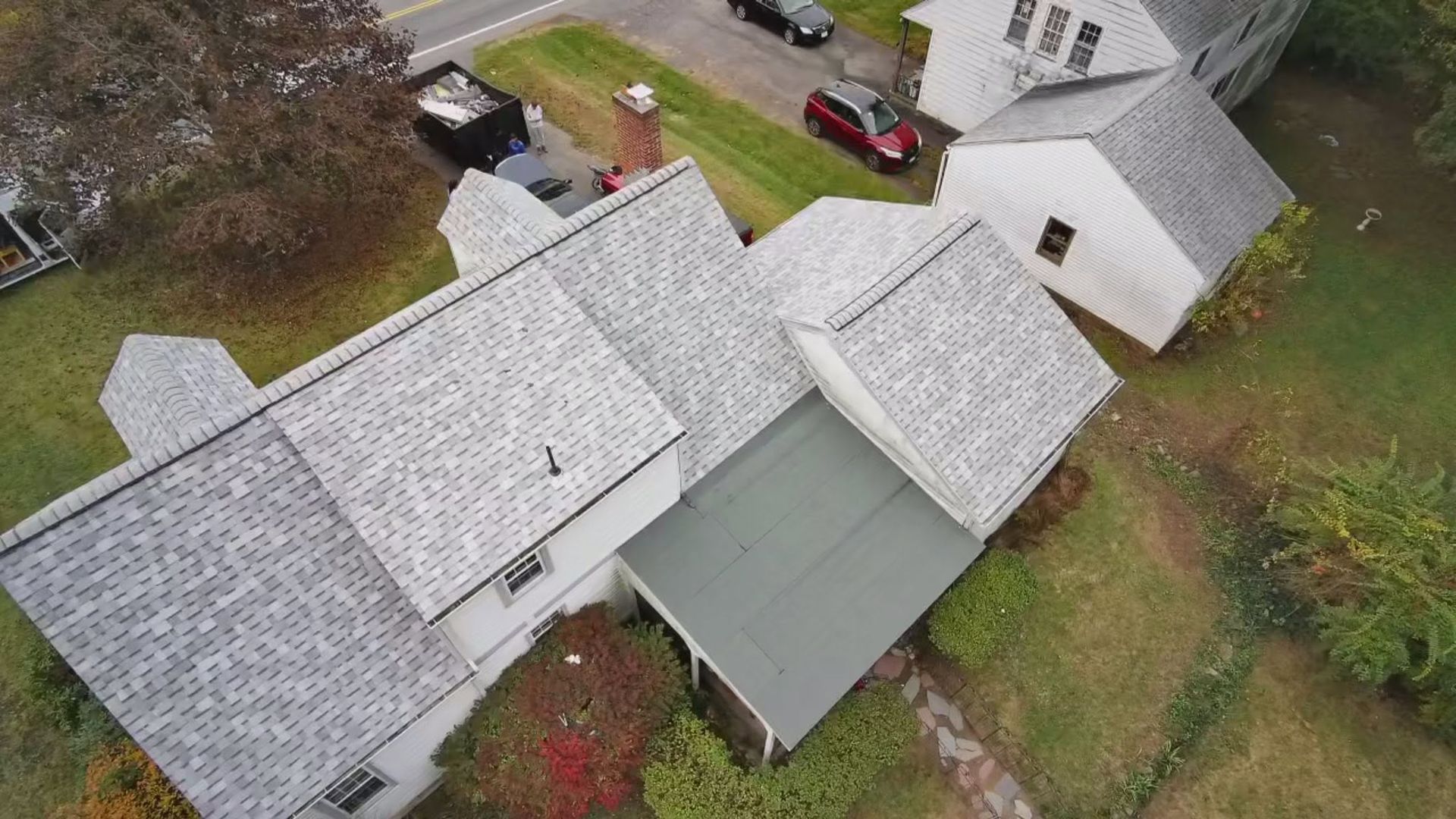 Aerial view of a gray-roofed house with a green carport beside a driveway and yard.