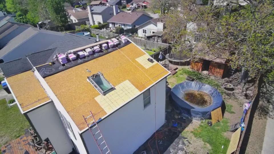 Aerial view of a house with a yellow roof, backyard, circular stone fire pit, and trees.