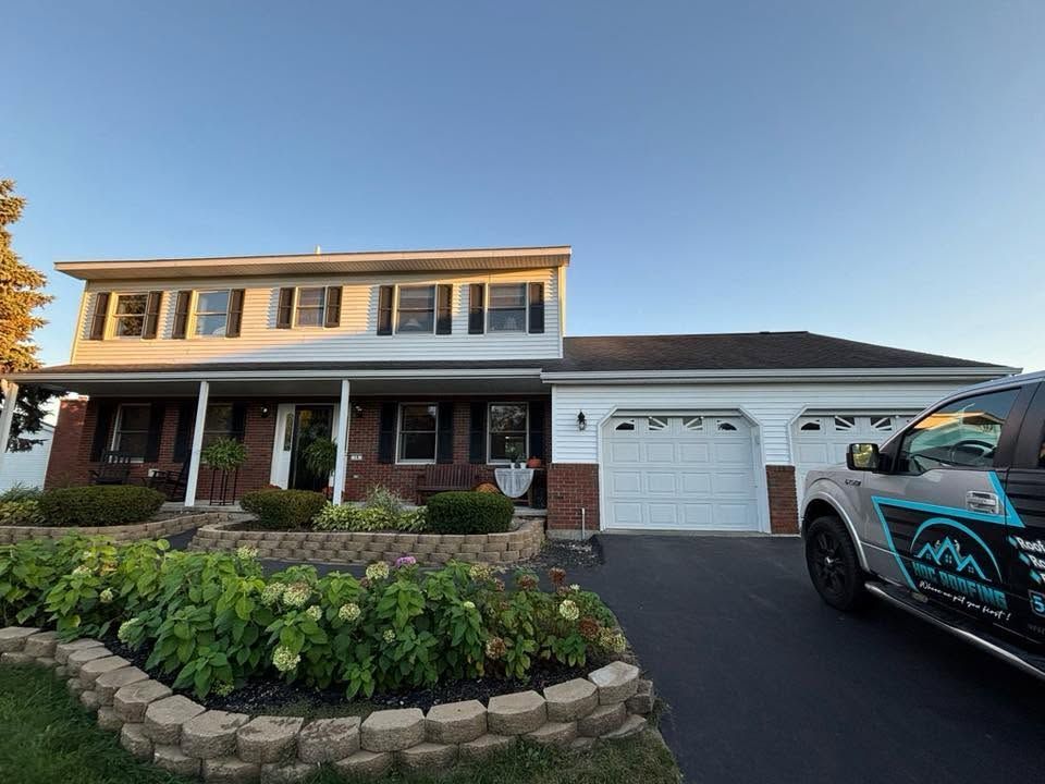 Suburban two-story house with brick porch, white garage, landscaped front yard, and a pickup truck in the driveway