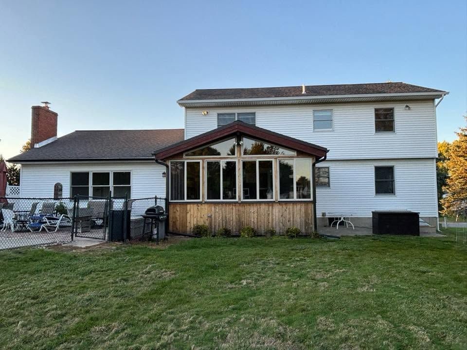 Large white house with a screened porch and patio on a grassy yard under a clear sky