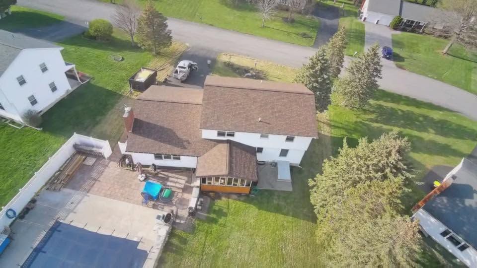 Aerial view of a suburban backyard with a house, deck, patio furniture, pool, and green lawn.