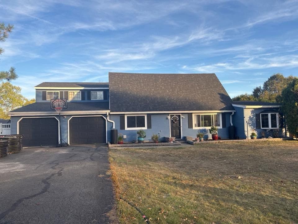 Suburban house with two-car garage, blue siding, and a large front lawn under a clear sky