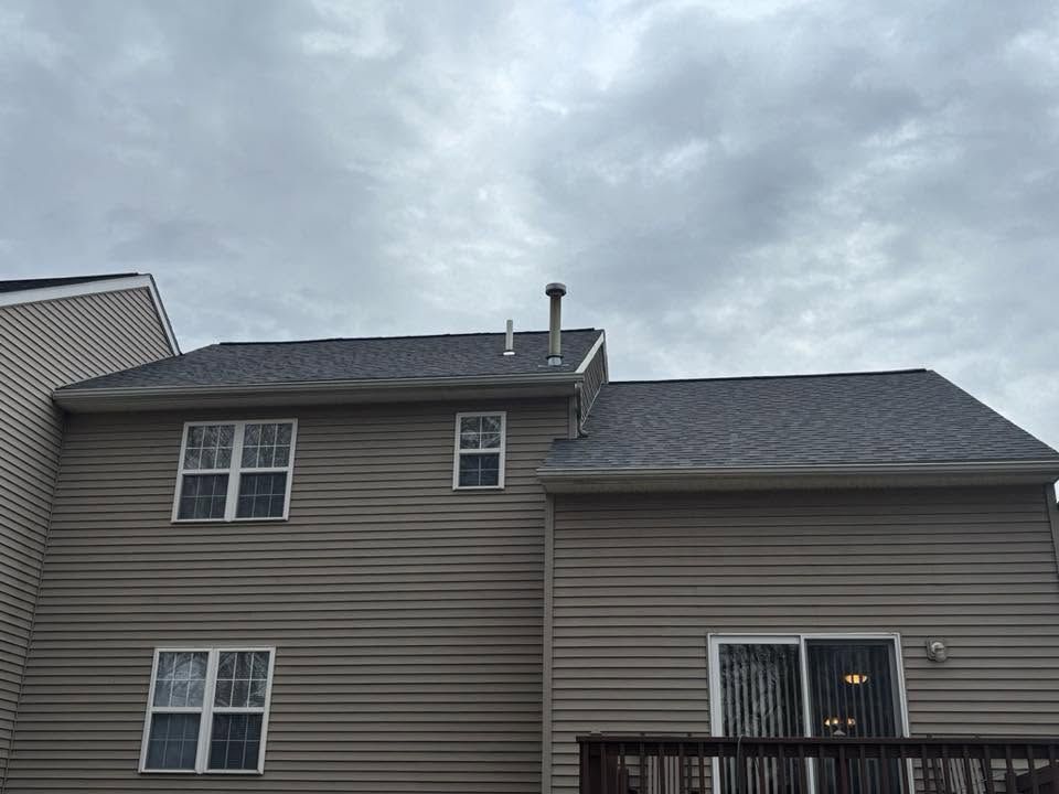 Two-story beige house with dark roof and cloudy sky overhead