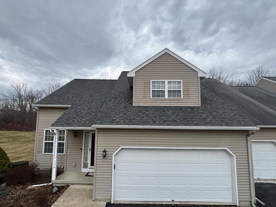 Suburban beige house with attached white garage under a cloudy sky
