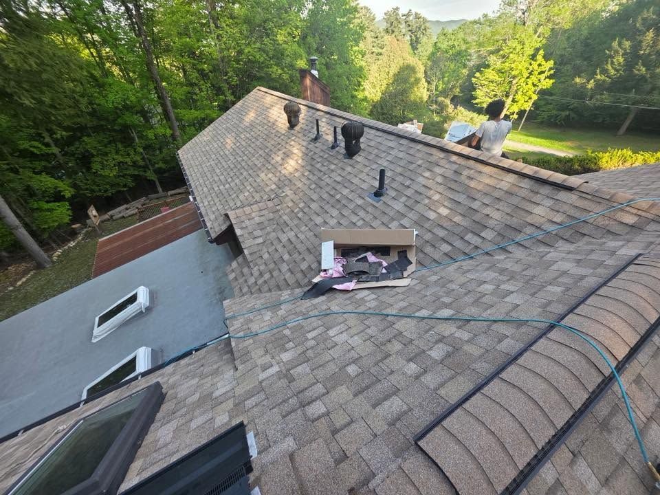 Roof repair on a gray shingled house, with workers near an open roof section.