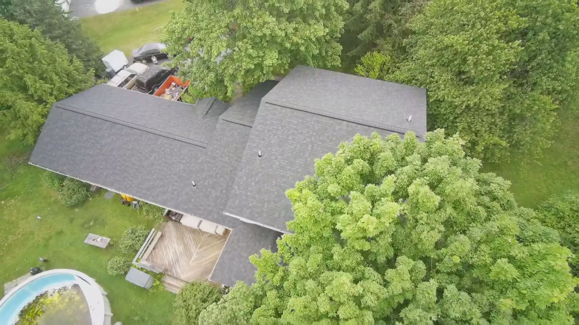Aerial view of a gray-roofed house surrounded by trees and a green lawn.
